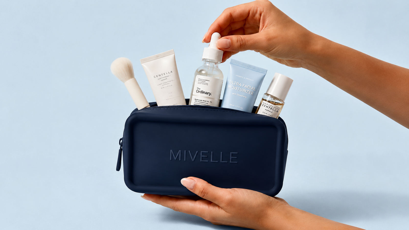 Hands holding a navy Mivelle skincare bag with curated products on a soft blue background